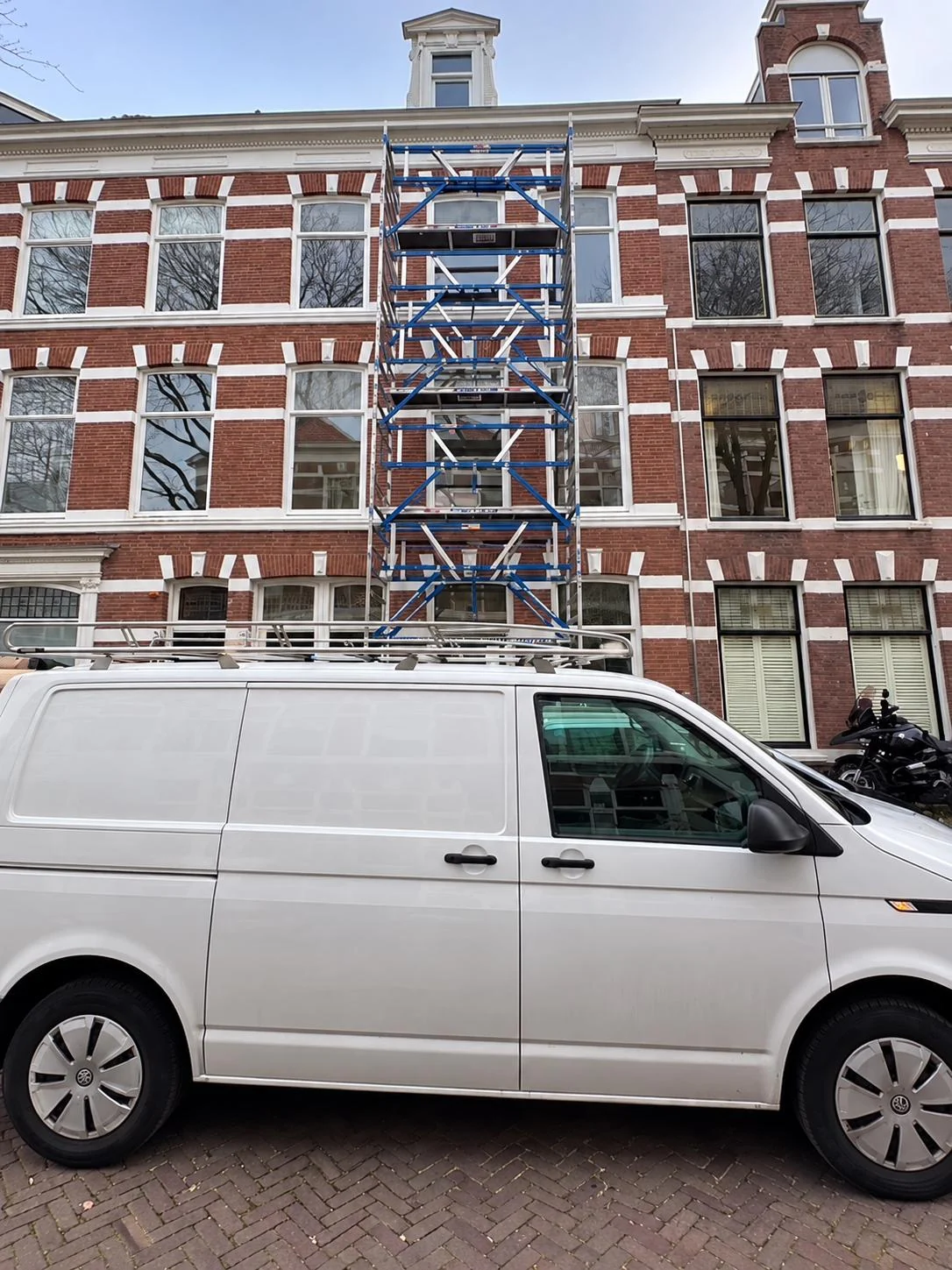 Bakstenen herenhuis met steiger aan de gevel en een witte werkbus ervoor