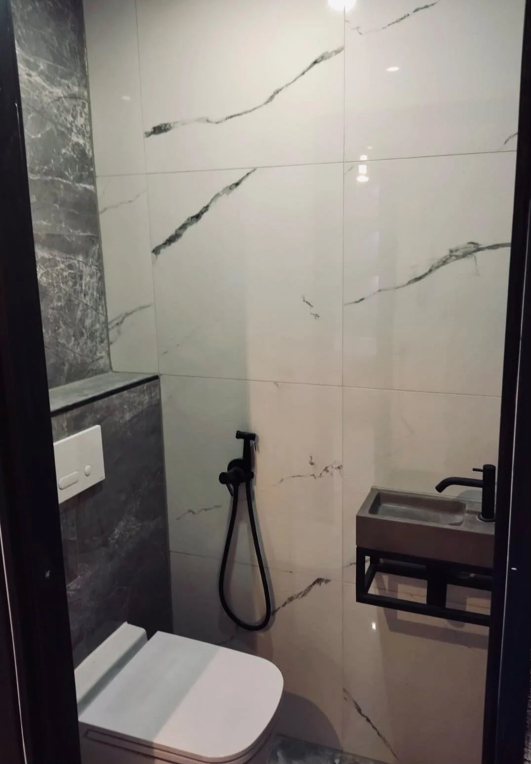 Toiletruimte met marmerlook tegels, zwevend toilet en zwarte kraan