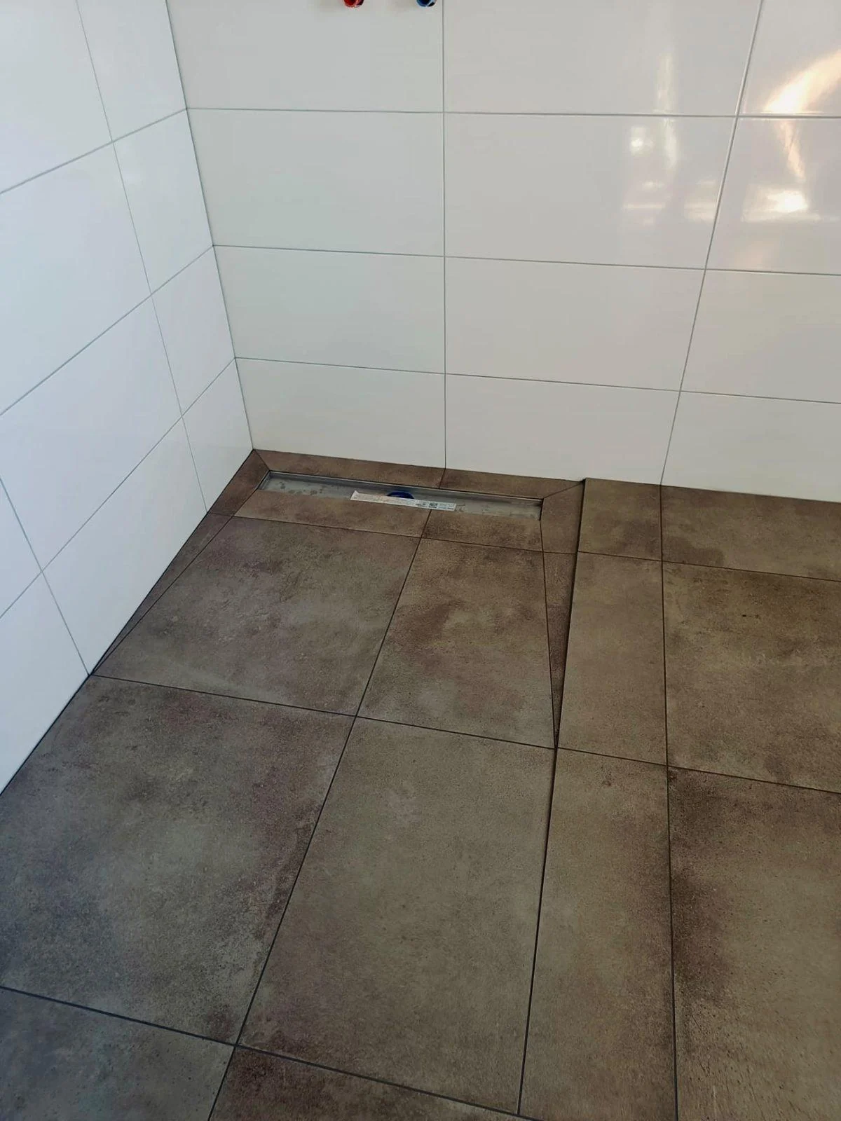 Afgewerkte badkamer met witte wandtegels, grote vloertegels en douchegoot
